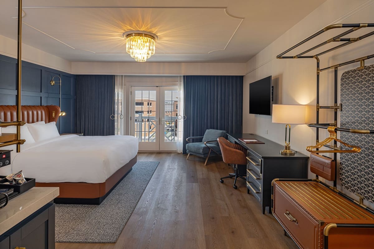 Ett hotellrum med en stor säng, ett skrivbord med en dator, en stol, en tv och en balkong med utsikt.