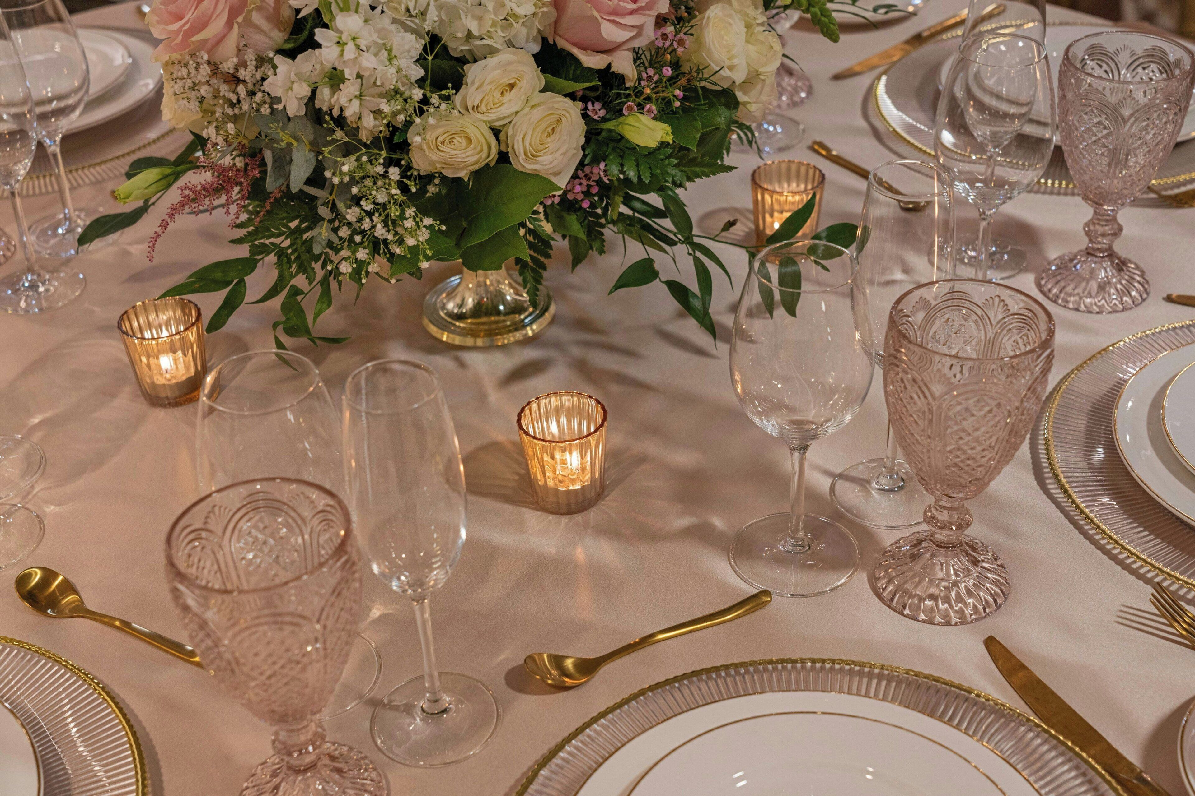 Una mesa dispuesta para un evento formal, con cristalería, cubiertos y un centro de mesa floral.