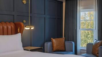 A hotel room with a bed, two armchairs, a nightstand, a lamp, and a window with curtains.