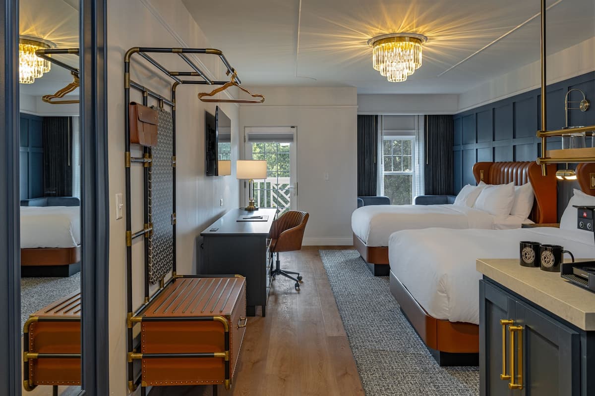 Ett hotellrum med två sängar, ett skrivbord, en stol, ett litet bord och en minibar.