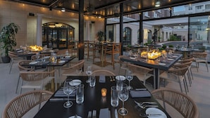 Un espace extérieur aménagé pour les repas, avec des tables et des chaises, un foyer et de grandes fenêtres donnant sur une cour intérieure.