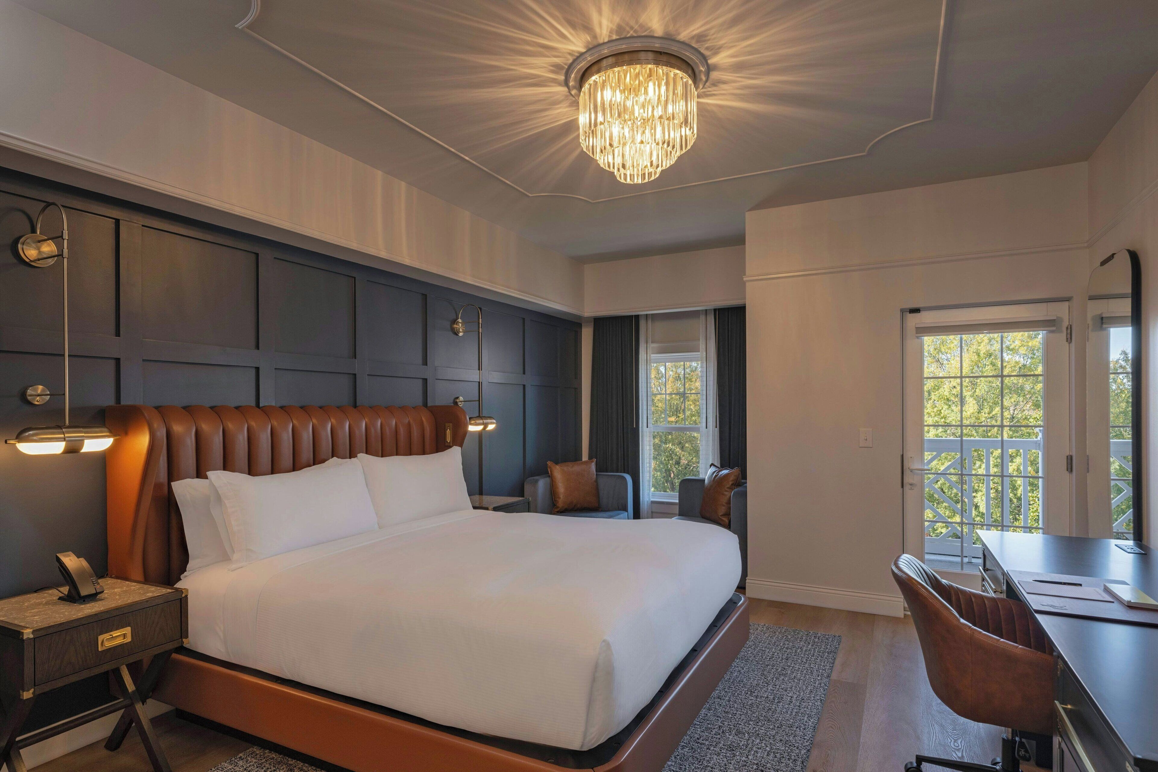 Una habitación de hotel moderna con una cama grande, un escritorio y una araña.