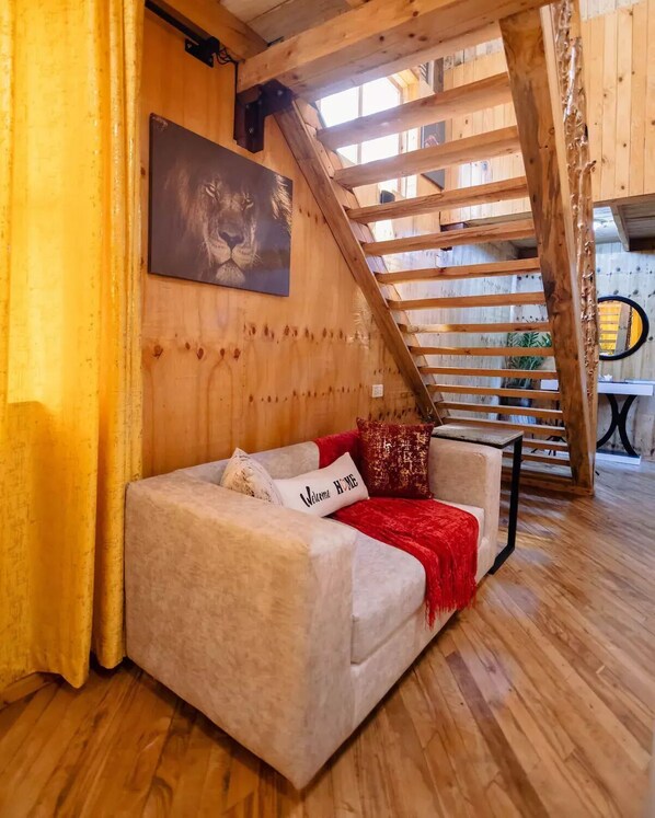 A cozy room with a wooden ceiling, a couch with a red throw blanket, and a 'Welcome Home' pillow. - The Wooden House
(Msaranga)