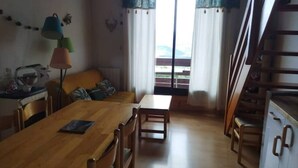 Un comedor con una mesa y sillas de madera, una lámpara y vistas al exterior a través de una ventana con cortinas.