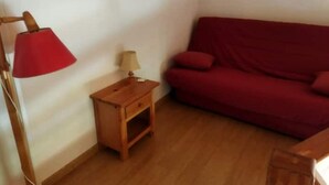 Una habitación con un sofá rojo, una mesita de noche de madera con una lámpara y una pequeña mesa.