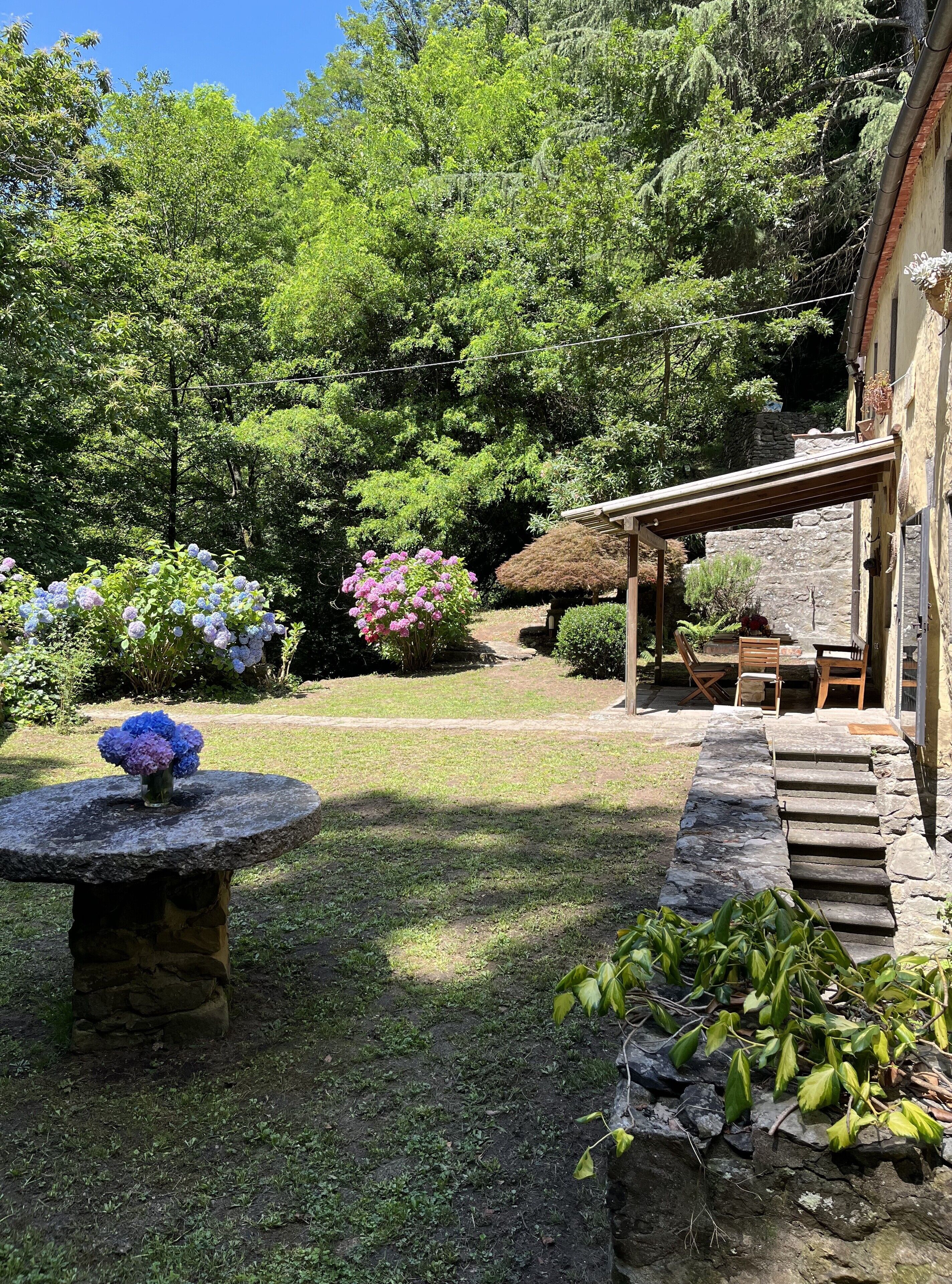A stone table with a vase of flowers in a garden area with a stone staircase leading to a wooden deck.