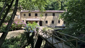 A rustic stone building with a tiled roof, surrounded by lush greenery and a wooden bridge. - Molin Barletta, Private Pool, Nature (Marliana)