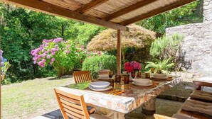 An outdoor dining area with a stone table and wooden chairs, surrounded by lush greenery and flowering plants. - Molin Barletta, Private Pool, Nature (Marliana)