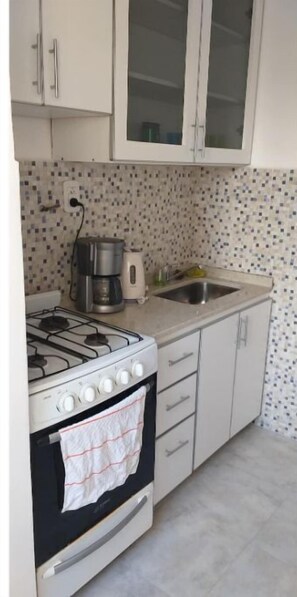A compact kitchen with a gas stove, oven, and a coffee maker. There is a sink and a tiled backsplash. - Cozy apartment in the Center of Buenos Aires (Buenos Aires)