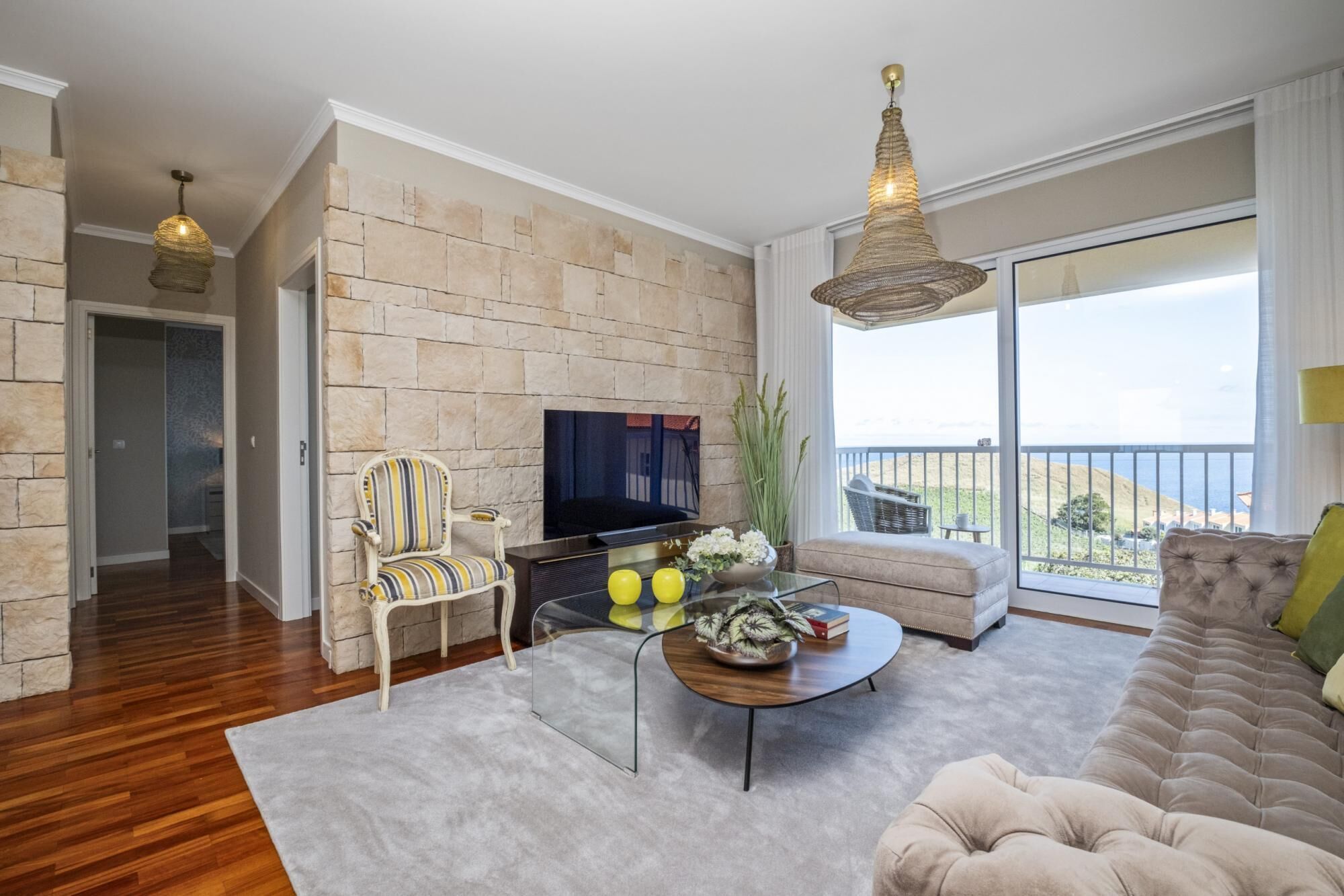 A living room with a stone wall, a sofa, a television, and a balcony with a view.