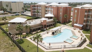 A hotel with multiple buildings, a central pool area with multiple pools, and a view of the ocean.