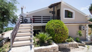 Un bâtiment à deux étages, avec un escalier menant à l’entrée, des unités de climatisation extérieures et une variété de plantes en pot.