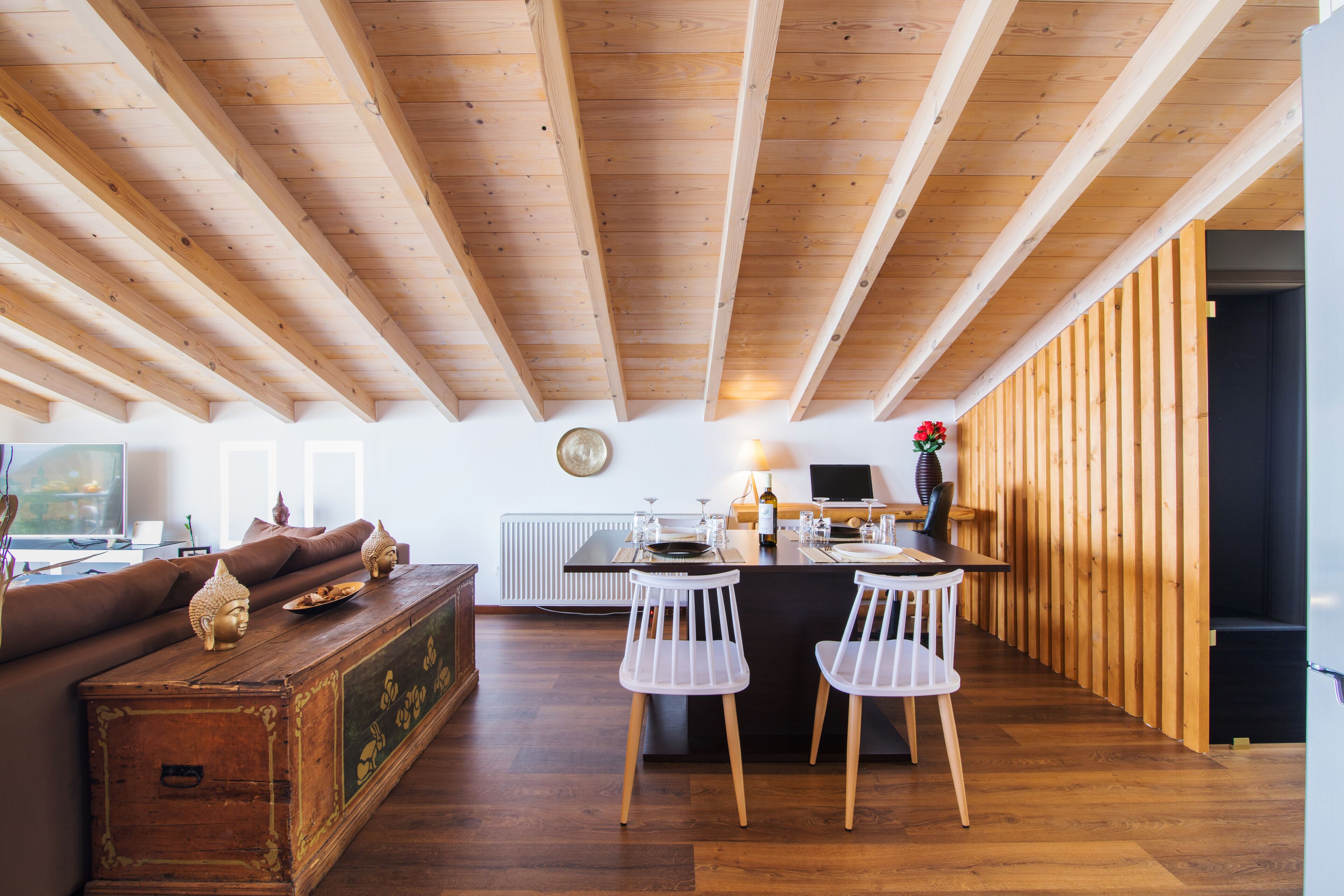 A modern kitchen with wooden beams, a dining area with white chairs, and a cozy seating area with a sofa and decorative items.