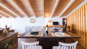 Une table de salle à manger en bois, des chaises, un téléviseur et un vase rempli de fleurs.