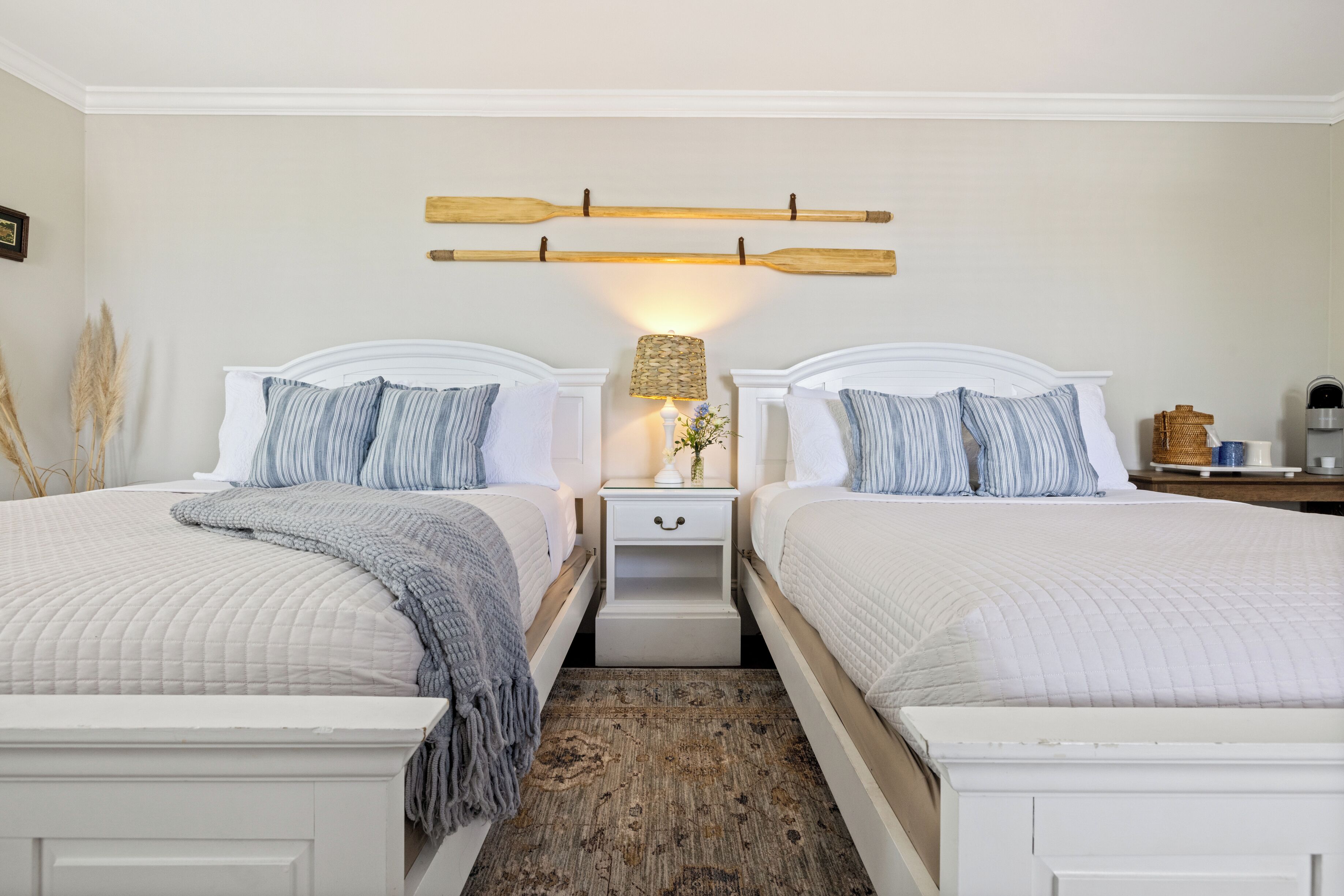 A double room with two beds, a nightstand with a lamp, and a wall-mounted wooden shelf.