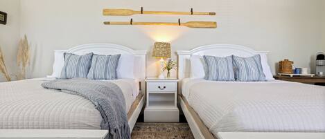 A double room with two beds, a nightstand with a lamp, and a wall-mounted wooden shelf.