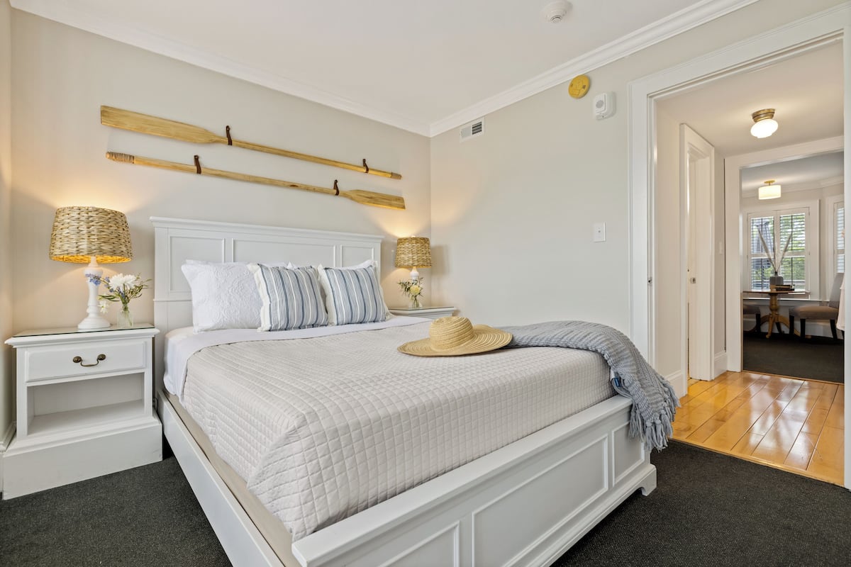 A neatly arranged bedroom with a large bed, white nightstands, and a wooden headboard.