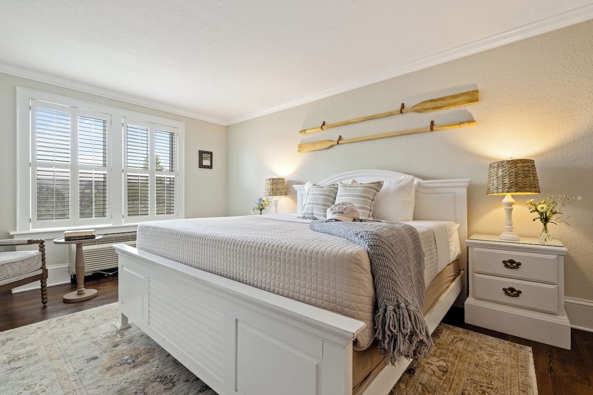 A bedroom with a large bed, bedside tables, a chair, and a window with blinds.