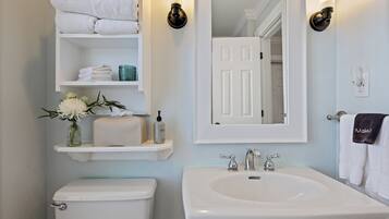 A bathroom with a toilet, sink, and shelves with towels and toiletries.