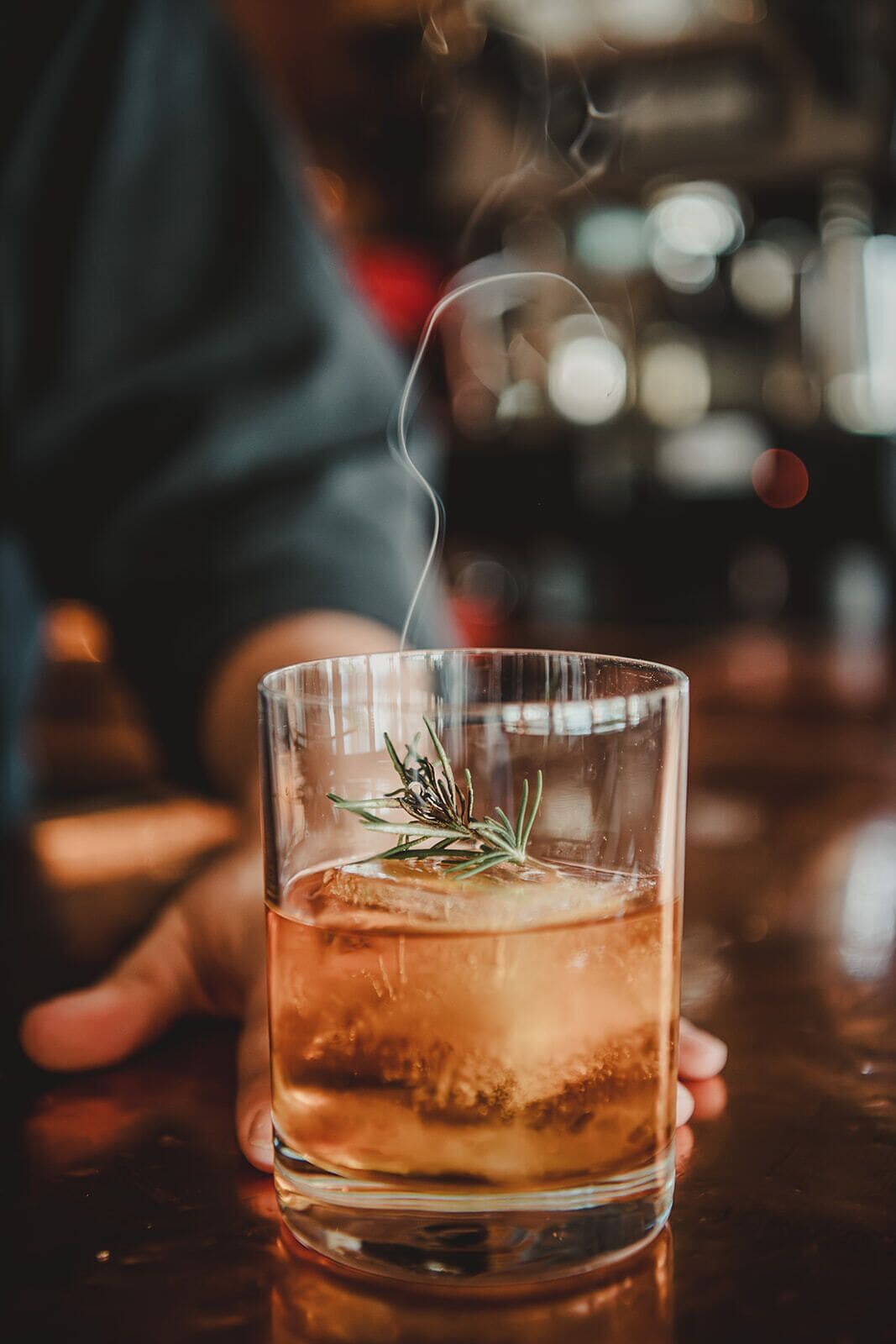 Ein klares Glas mit Flüssigkeit, Eiswürfeln und einem Rosmarinzweig.