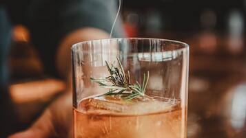 Ein klares Glas mit Flüssigkeit, Eiswürfeln und einem Rosmarinzweig.