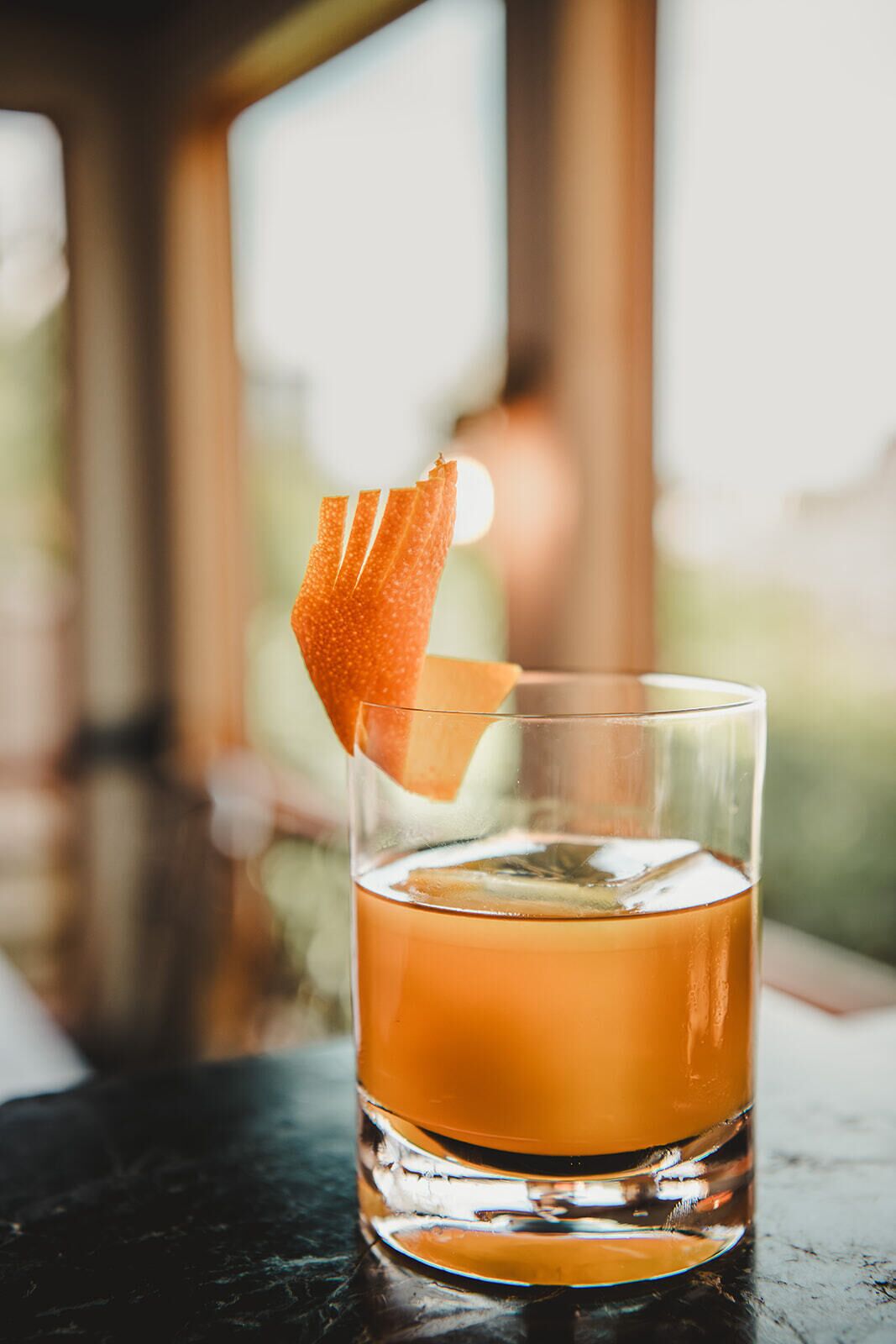 A glass of amber-colored beverage with a citrus garnish on a bar counter.