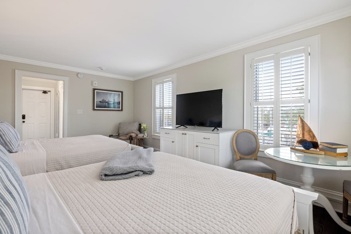 A hotel room with two beds, a television, a chair, and a table with a sailboat model.
