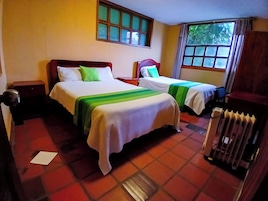 Una habitación de hotel con dos camas, una ventana con cortinas, un radiador y una mesita de noche.