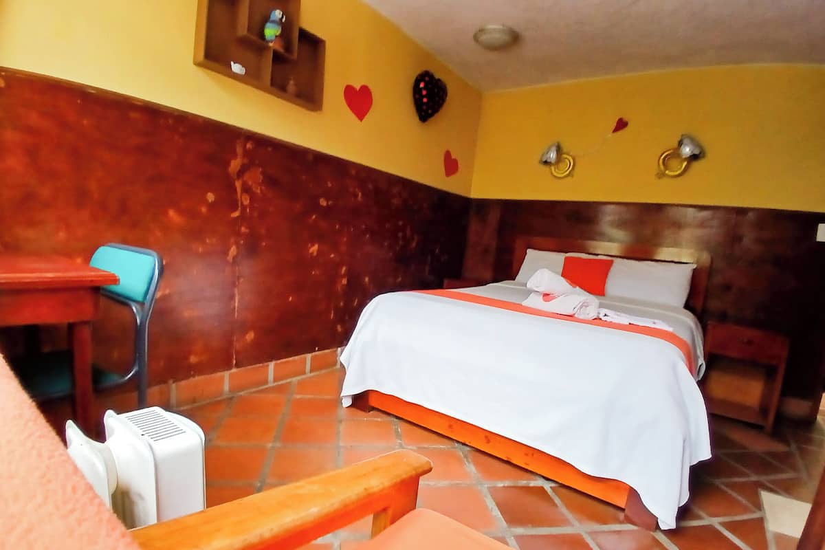 Une chambre d’hôtel comprenant un lit, un bureau, une chaise et une petite étagère ornée d’objets décoratifs.