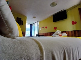 Habitación de hotel con cama, televisor montado en la pared y ventana con vistas.