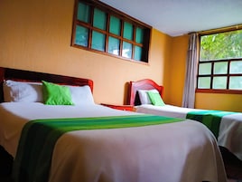 Habitación de hotel con dos camas, cada una con cabecero de madera y cubrecamas verdes. Se ve vegetación a través de la ventana.