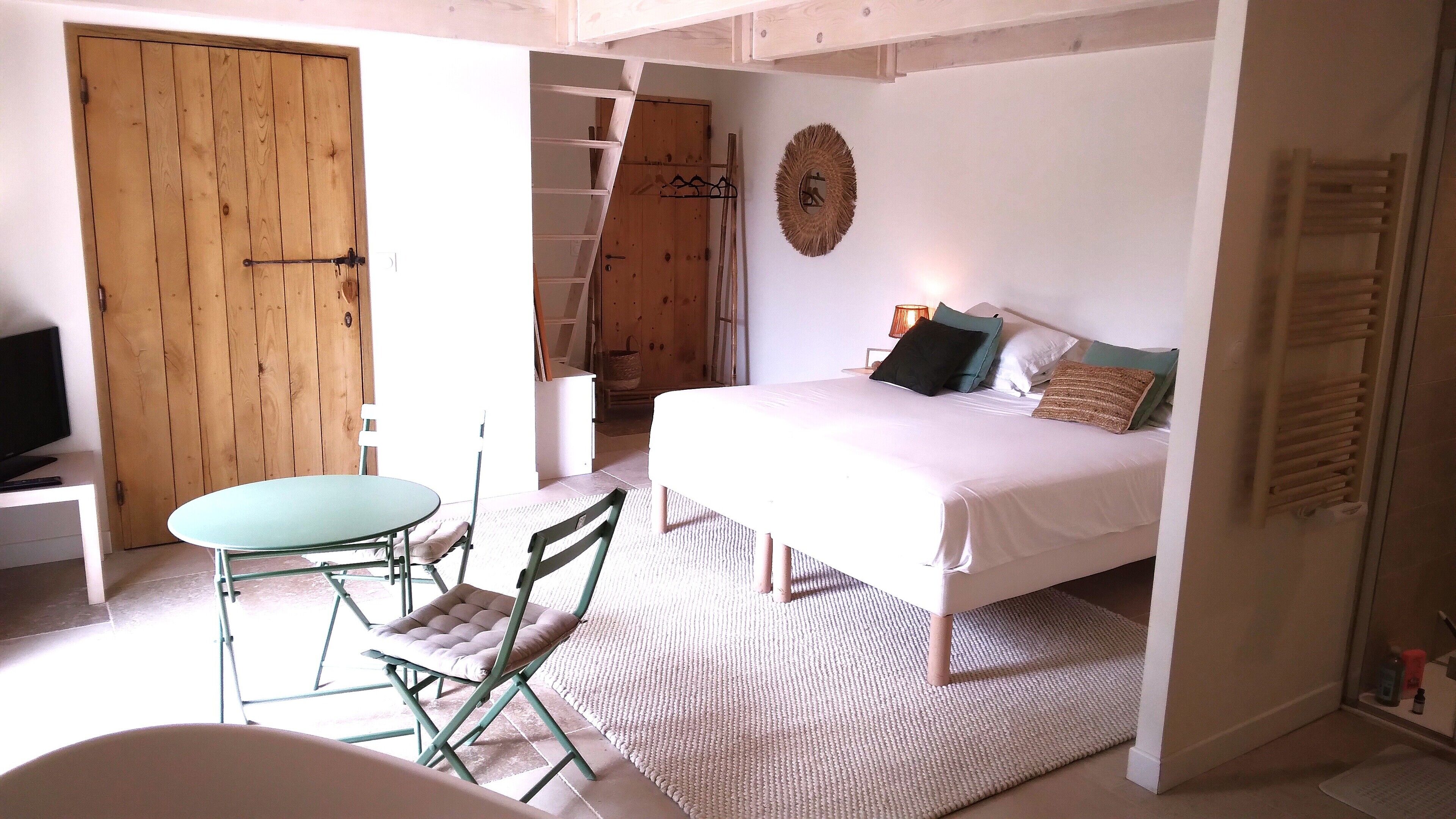 A bedroom with a bed, a chair, a small table, a wooden wardrobe, and a ladder.