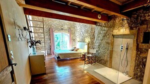 A bedroom with a stone wall, wooden flooring, a bed, a bedside table, and a shower area.