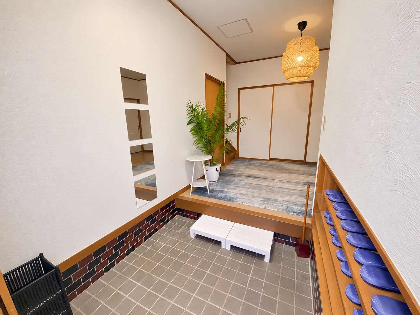 A hotel room with a wooden bench, a potted plant, a wall-mounted shelf, and a seating area with blue chairs.