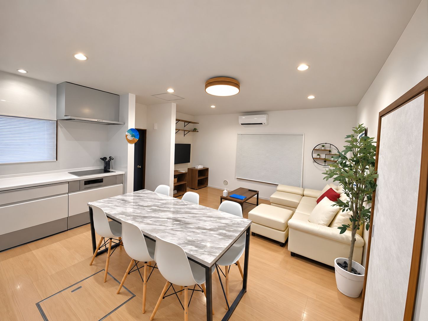 Un espacio habitable moderno con cocina, comedor y zona de estar con sofá y planta en maceta.