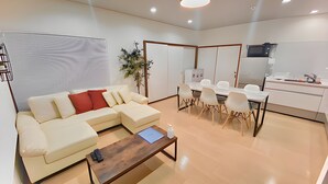 A modern living room with a sectional sofa, a coffee table, and a dining area with chairs and a table. - Eternity Marina HOUSE Onjuku (Onjuku)