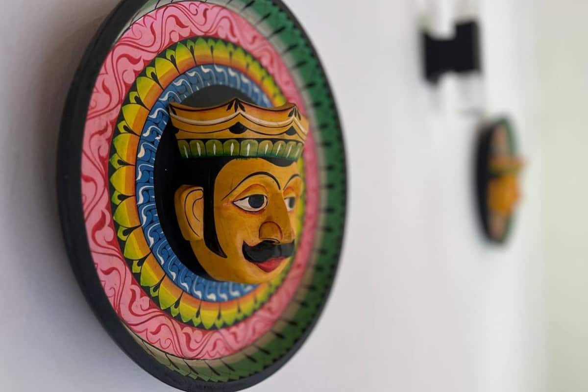 Un objeto circular y colorido con un diseño facial, posiblemente un adorno o una máscara, fijado en una pared.
