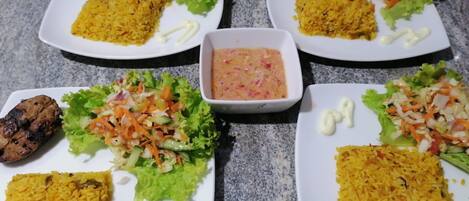 Quatre assiettes garnies de viande grillée, de riz jaune et d’une salade, accompagnées d’un petit bol de sauce.