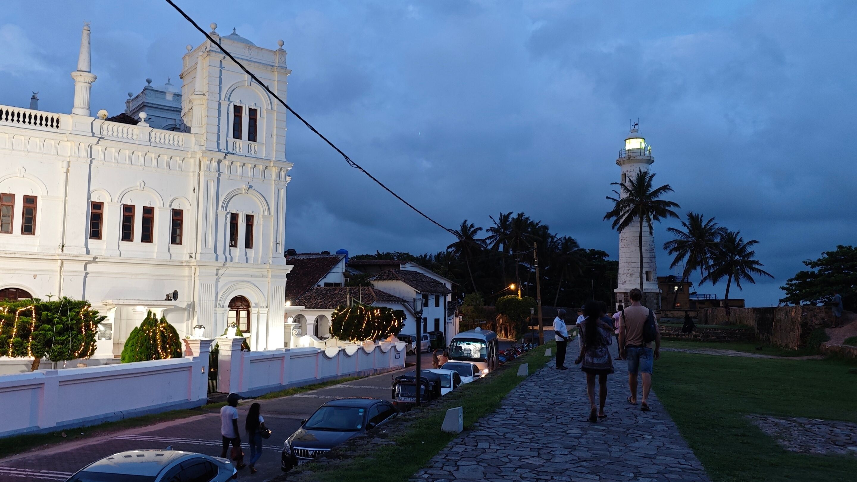 A historic building with classical architecture, a paved pathway, and palm trees.