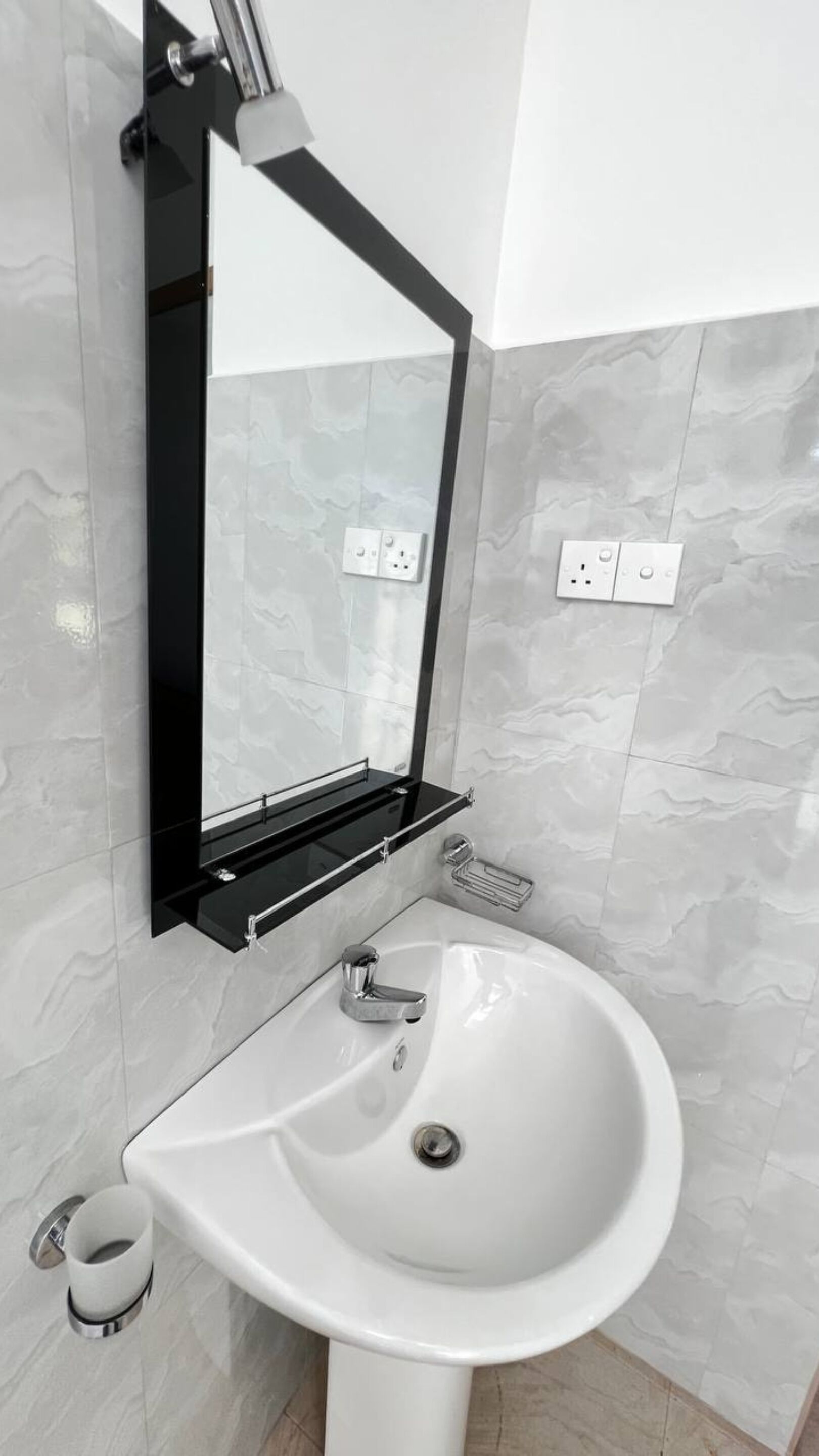 Ein modernes Badezimmer mit einem weißen Waschbecken, einem schwarzen Spiegel und Wänden mit Marmoroptik.