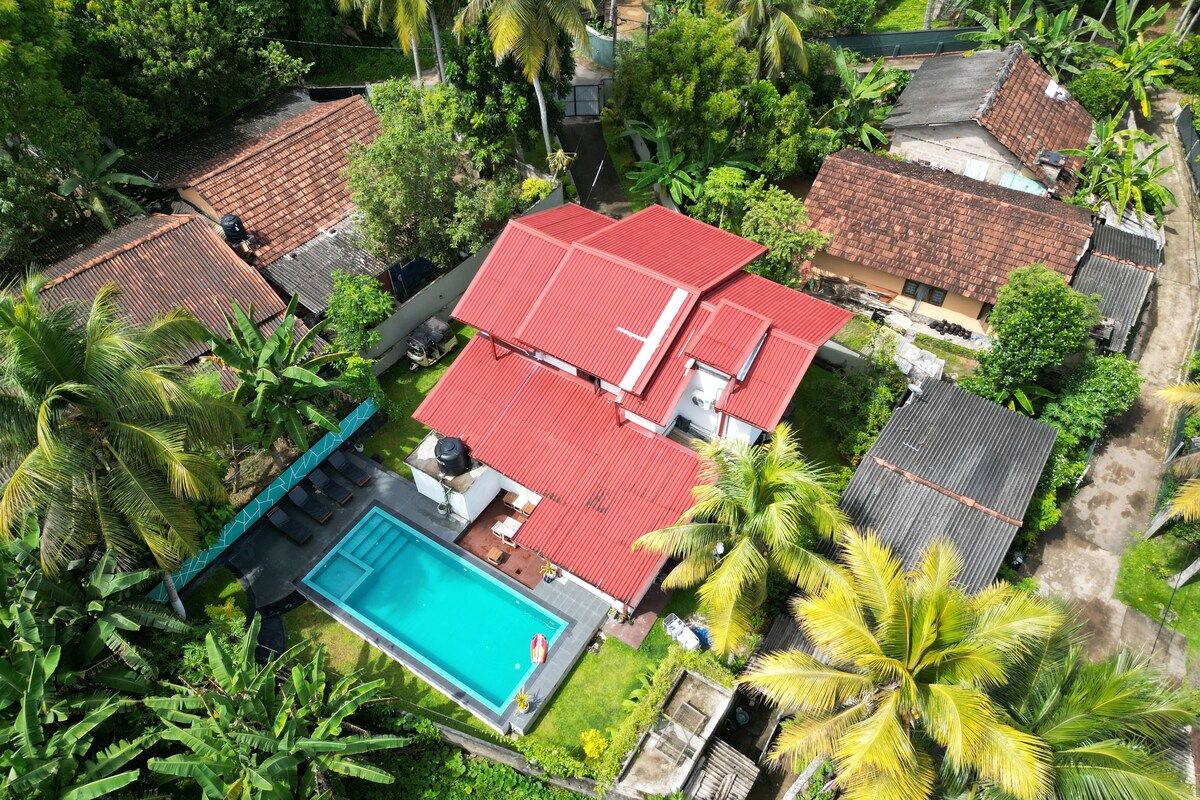 An aerial view of a residential area with multiple houses, a swimming pool, and lush greenery.
