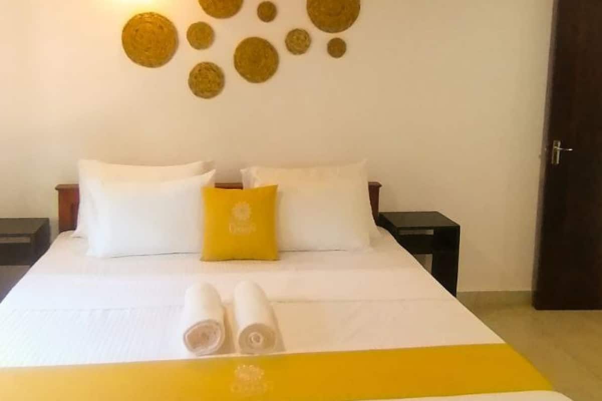 Una cama bien hecha con ropa de cama blanca y amarilla, dos almohadas blancas y una almohada de color amarillo. Hay dos mesitas de noche con lámparas, y se ve una puerta a la derecha.