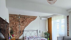 A spacious loft bedroom with a large bed, a modern ceiling light, and a brick wall. - Urban Cozy Retreat (Pristina)