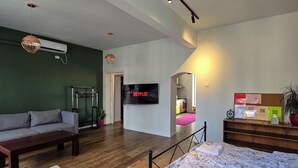 A modern living room with a sofa, a coffee table, a bed with a floral bedspread, a flat-screen TV, and a staircase leading to another room. - Urban Cozy Retreat (Pristina)