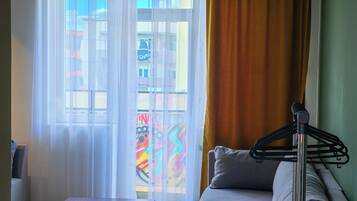 Una sala de estar con sofá, mesa de centro, lámpara colgante, cortinas translúcidas y vistas de edificios a través de una ventana.