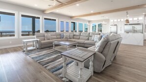 Ein geräumiges Wohnzimmer mit einer großen Eckcouch, einem Couchtisch und Meerblick durch große Fenster.