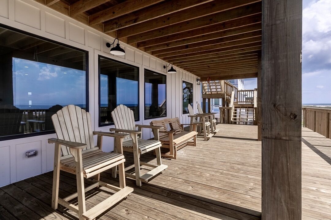 Een houten terras met Adirondack-stoelen en grote ramen met uitzicht op de oceaan.