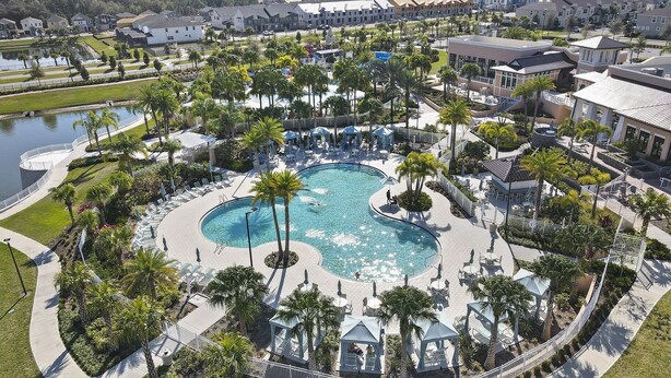 Eine Luftaufnahme eines Resorts mit einem zentralen Schwimmbecken, umgeben von Palmen, Liegestühlen und einer kleinen Laube.
