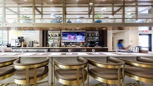Eine Bar mit einer langen Theke, mehreren Barhocker und einem Fernsehbildschirm, der eine Sportveranstaltung zeigt.
