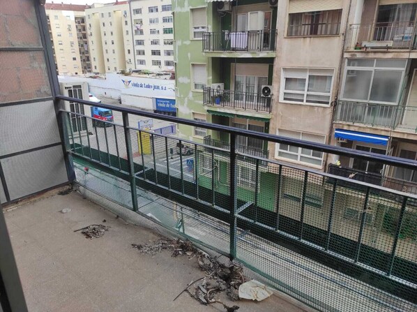 Ein Balkon mit Metallgeländer, der auf eine Straße mit Gebäuden und einem parkenden Lieferwagen blickt.